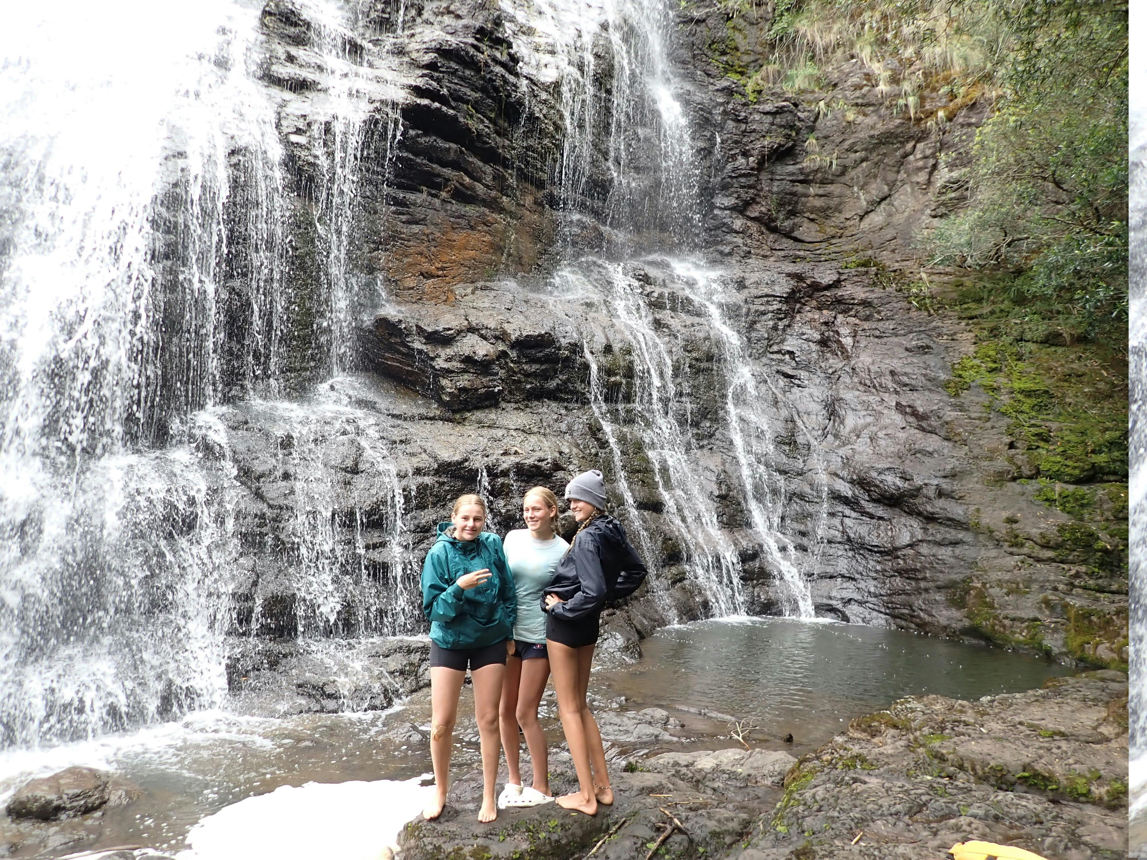 Three girls are standing at the base of a waterfall on the Snowy River rafting trip