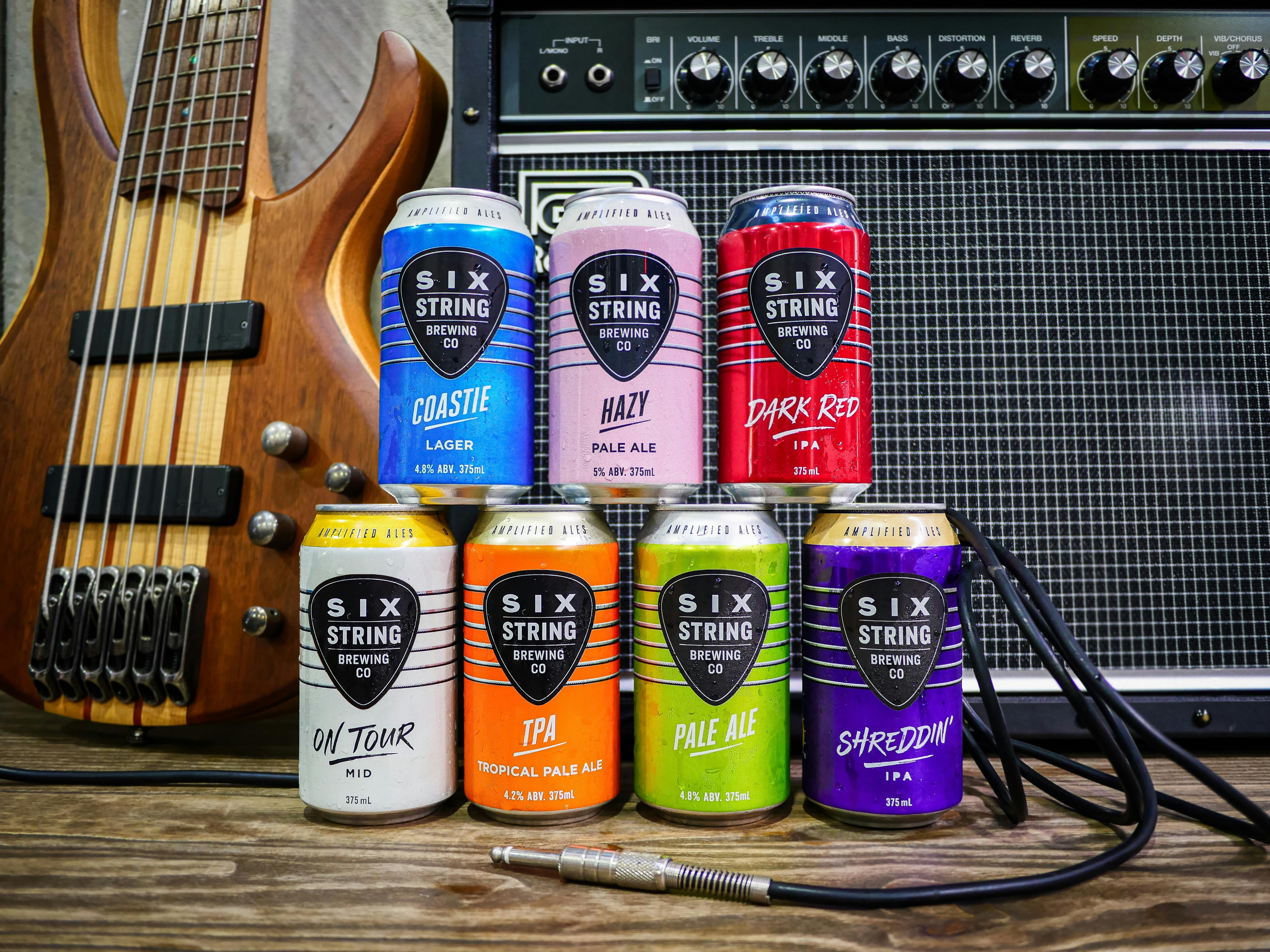 7 Core Range beer cans sitting on top of a table with a guitar amplifier and bass amp behind it.