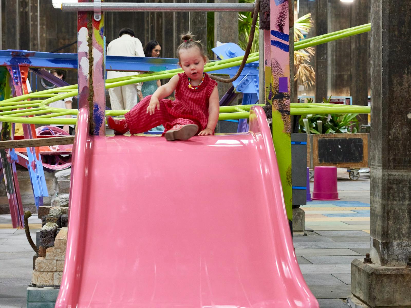 A child in a red outfit is about to slide down a slide in an underground art gallery space