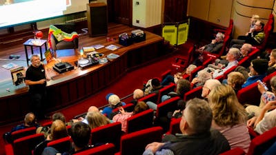 Audience in a theatre and a man at the front preparing to play a vinyl