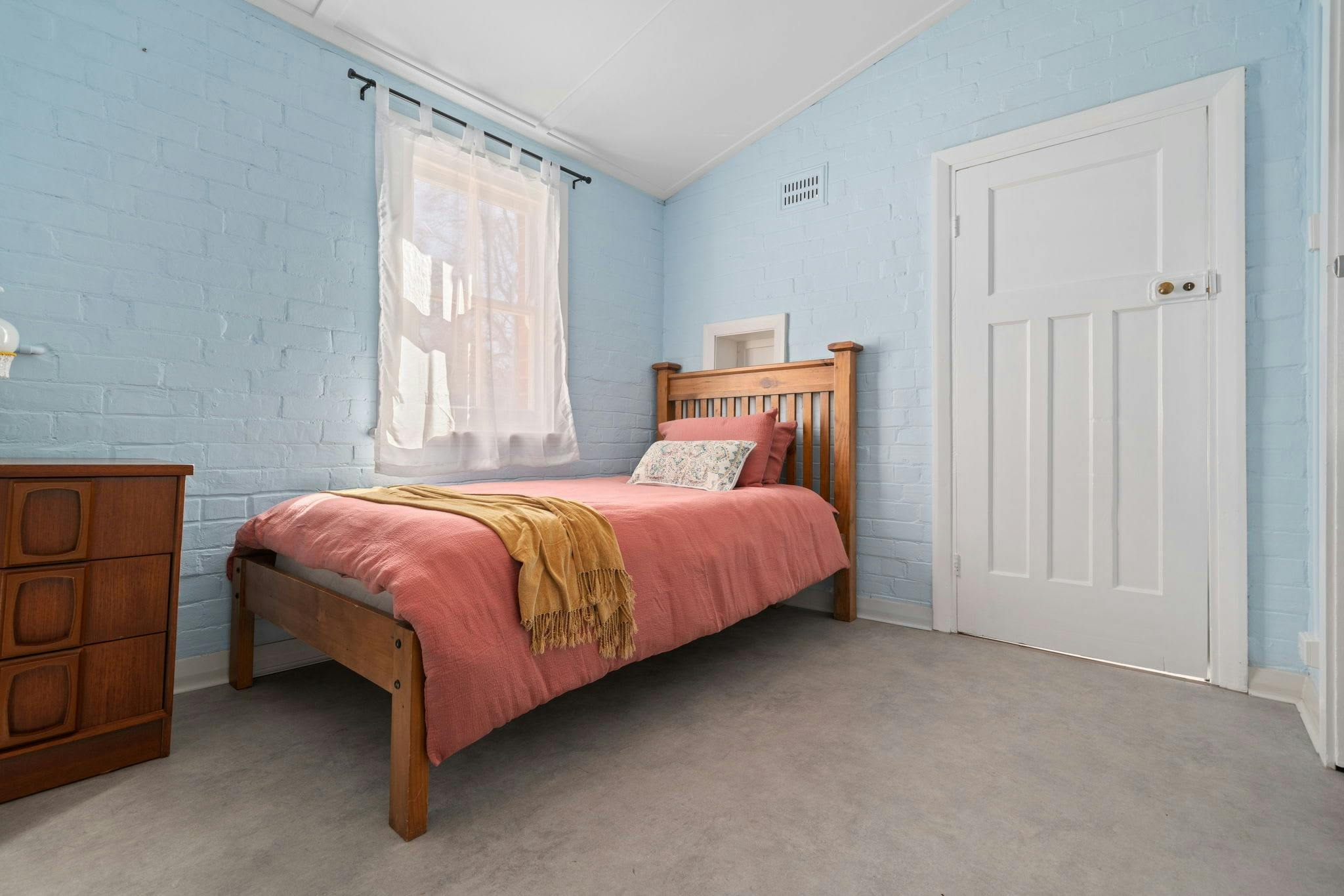 ピンクの毛布、黄色のひざ掛け、青い壁のキングサイズのシングルベッド。