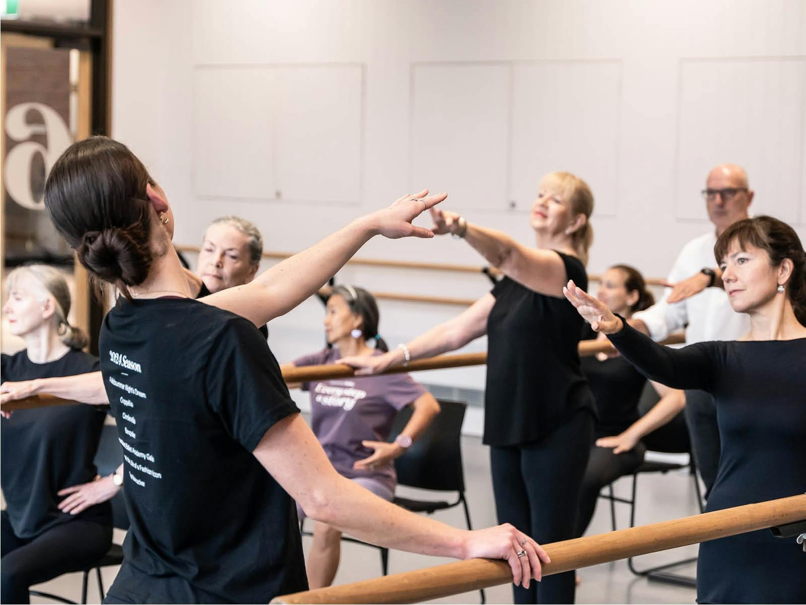 Ballet class for adults, some standing at the barre, and others seated focusing on arm positioning Ballet class for adults, some standing at the barre, and others seated focusing on arm positioning