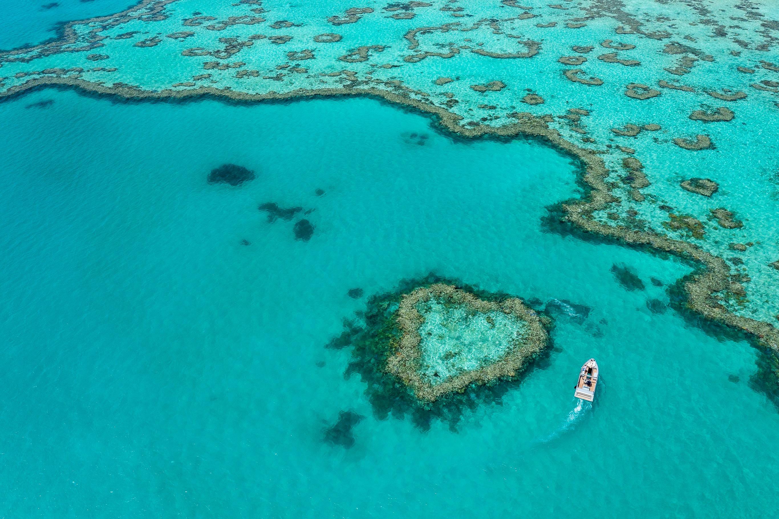 Aerial photo of heart reef with small boat going around the reef and turquoise waters