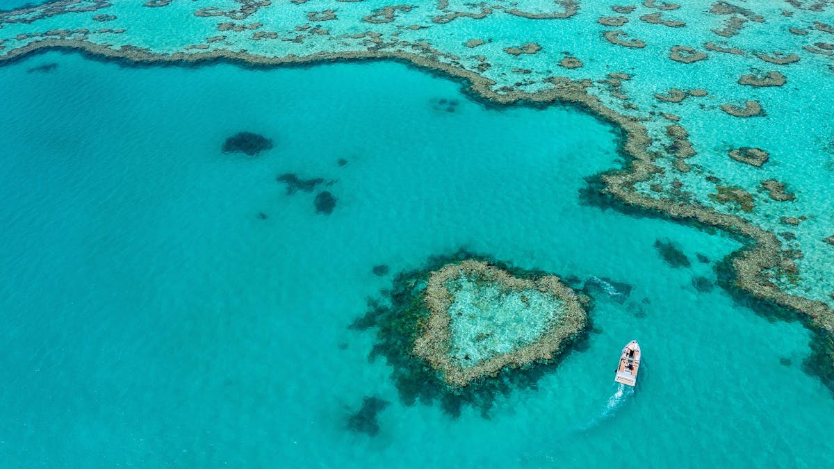 Aerial photo of heart reef with small boat going around the reef and turquoise waters