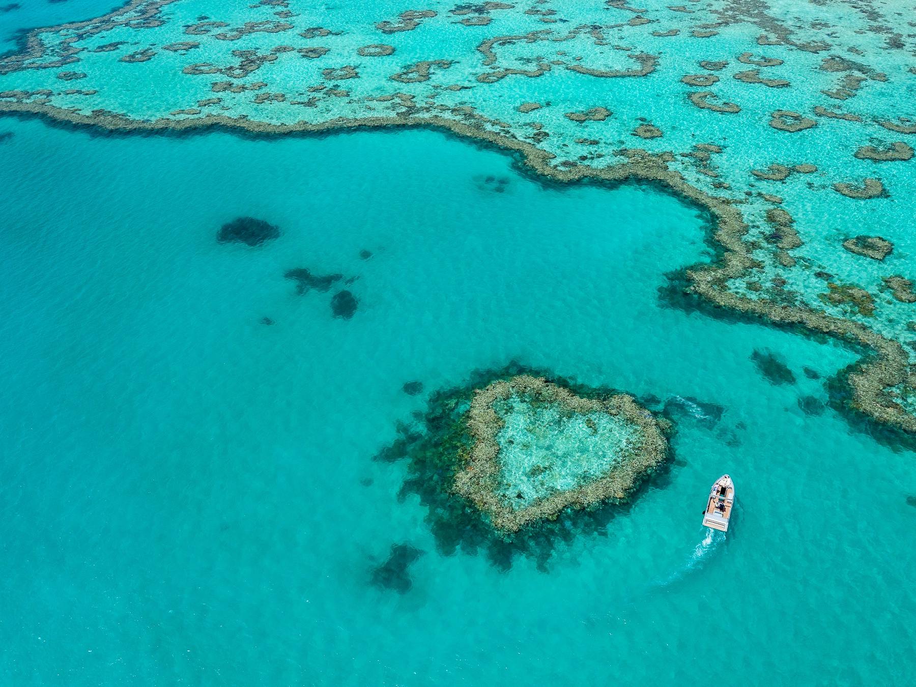 Aerial photo of heart reef with small boat going around the reef and turquoise waters