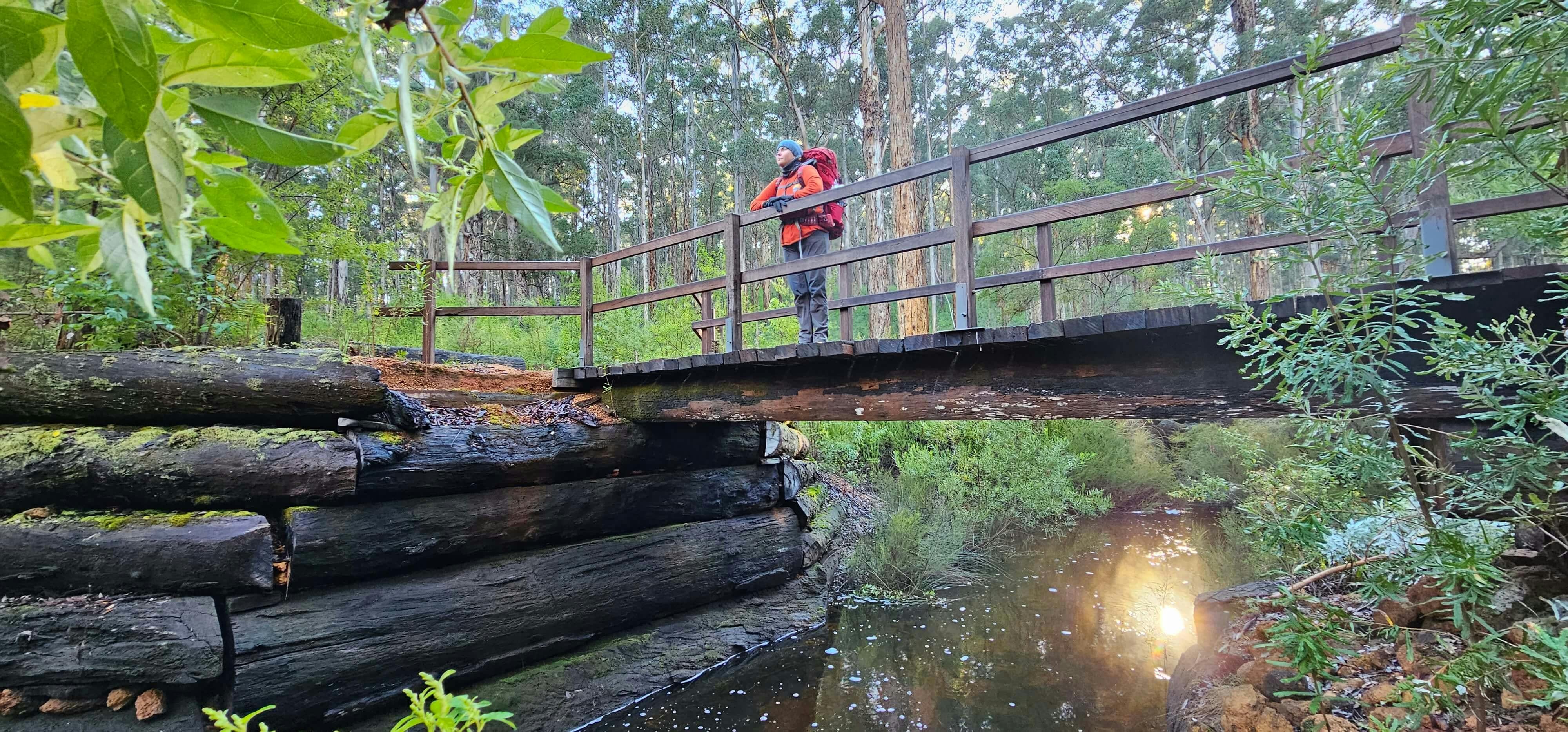 Hiker standing on bridge looking outwards while warm sunshine reflects on water