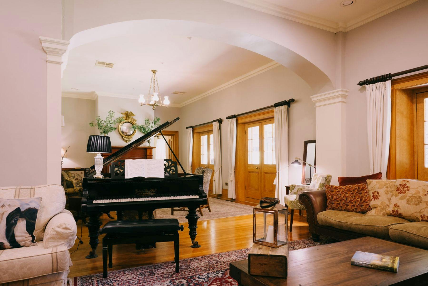 An elegant living room featuring a grand piano, cozy seating, warm wood tones, and classic decor.