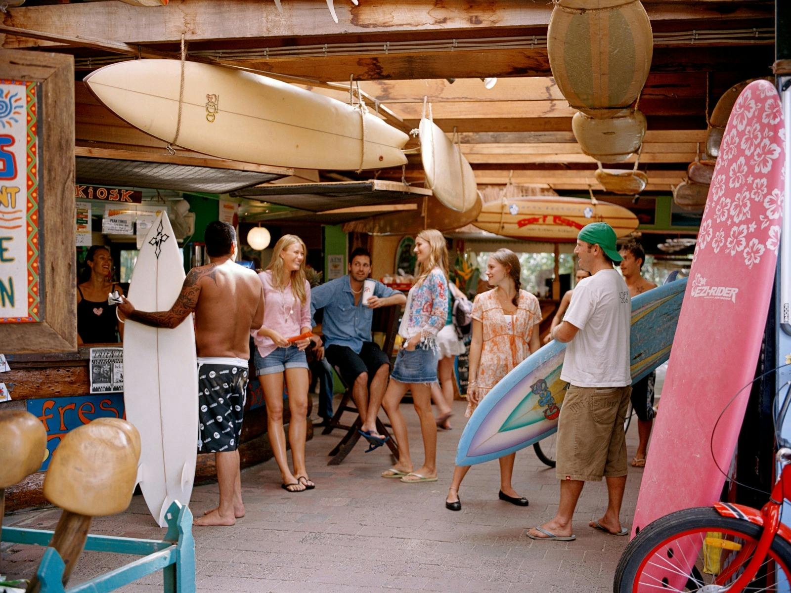 A group of young people gather in a backpackers laughing and holding surfboards