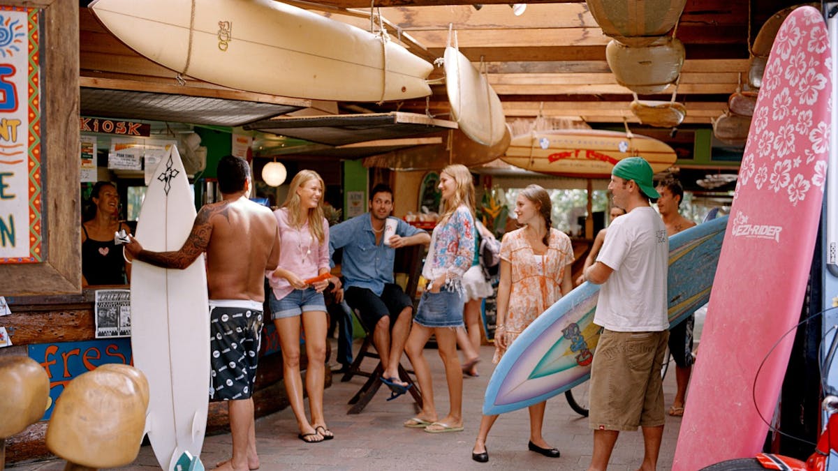 A group of young people gather in a backpackers laughing and holding surfboards