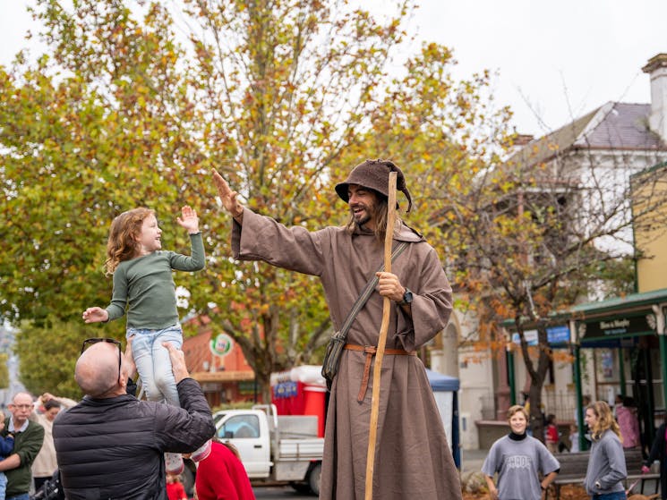 A child high is lifted to high five a stilt walker dressed as a wizard