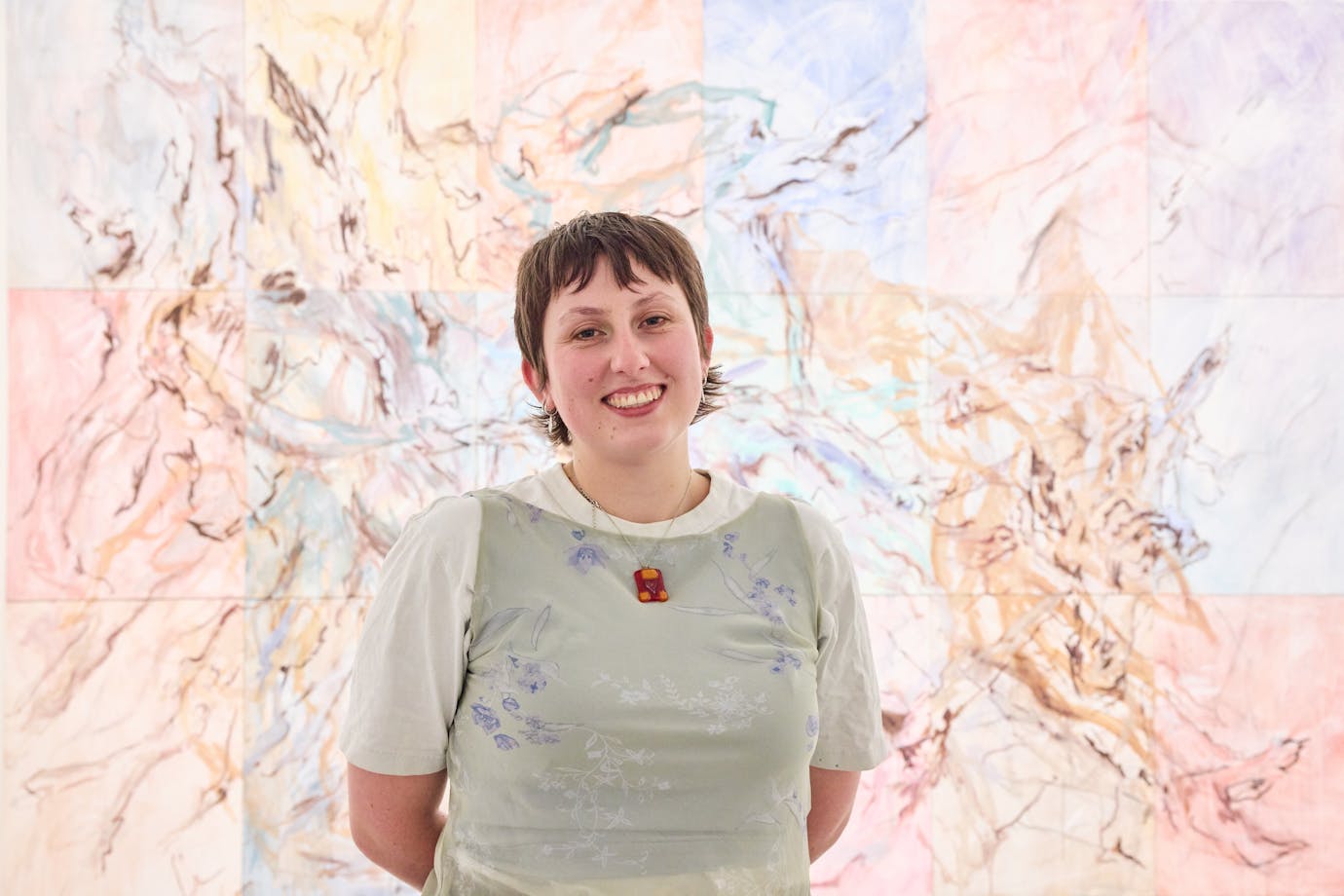 Sarah Murray smiling, stands in front of an exuberant abstract painting.