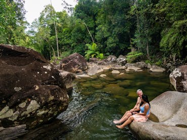 Couple sitting on creek boulders on crystal clear creek