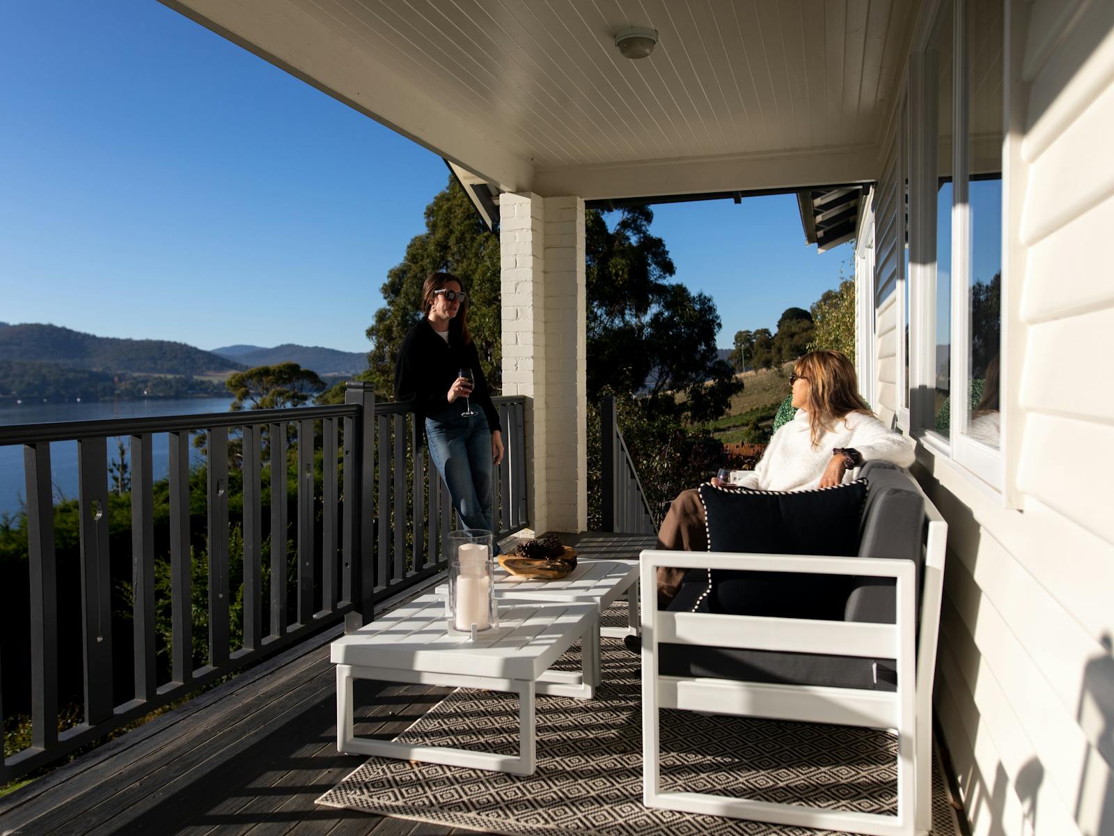 Image of two people holding a drink on a balcony with the view of the water