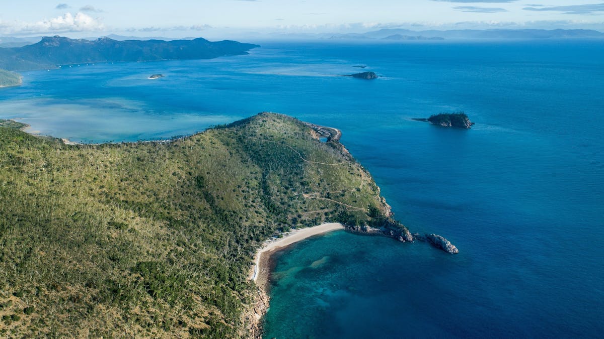 Aerial photo of secluded beach and island greenery with other islands in the distance in the ocean.