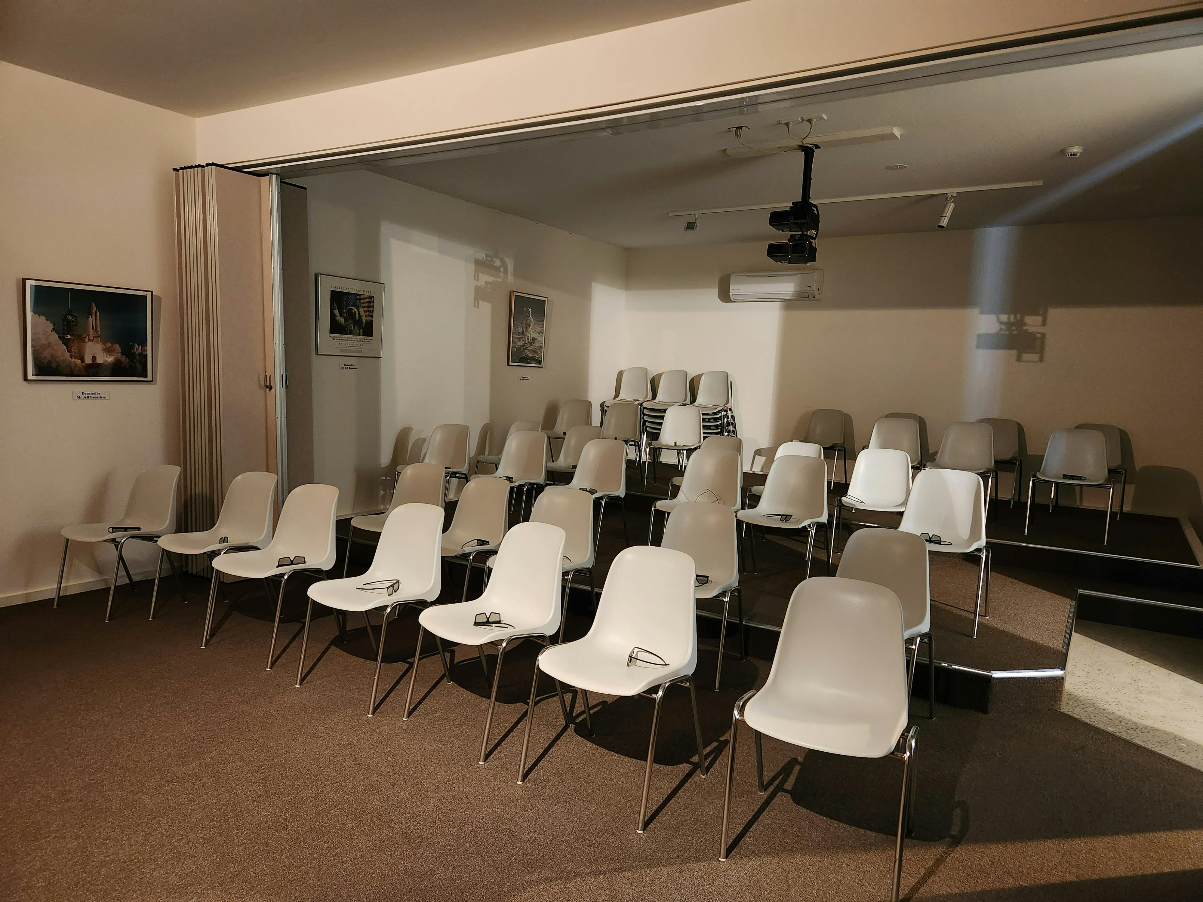 Virtual reality theatre filled with chairs and 3D glasses. There are two video projectors as well.