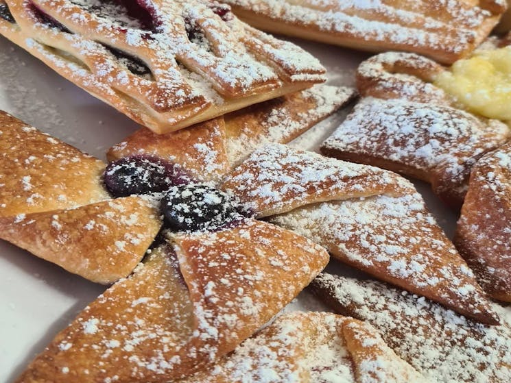 Various Danishes covered in icing sugar, some with berries and some with chocolate.