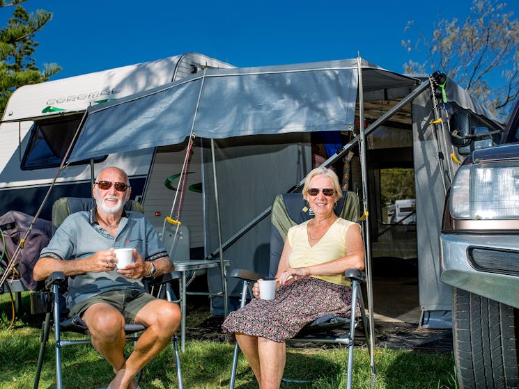 Couple sitting in front of caravan on holiday at Reflections Holiday Parks Corindi Beach