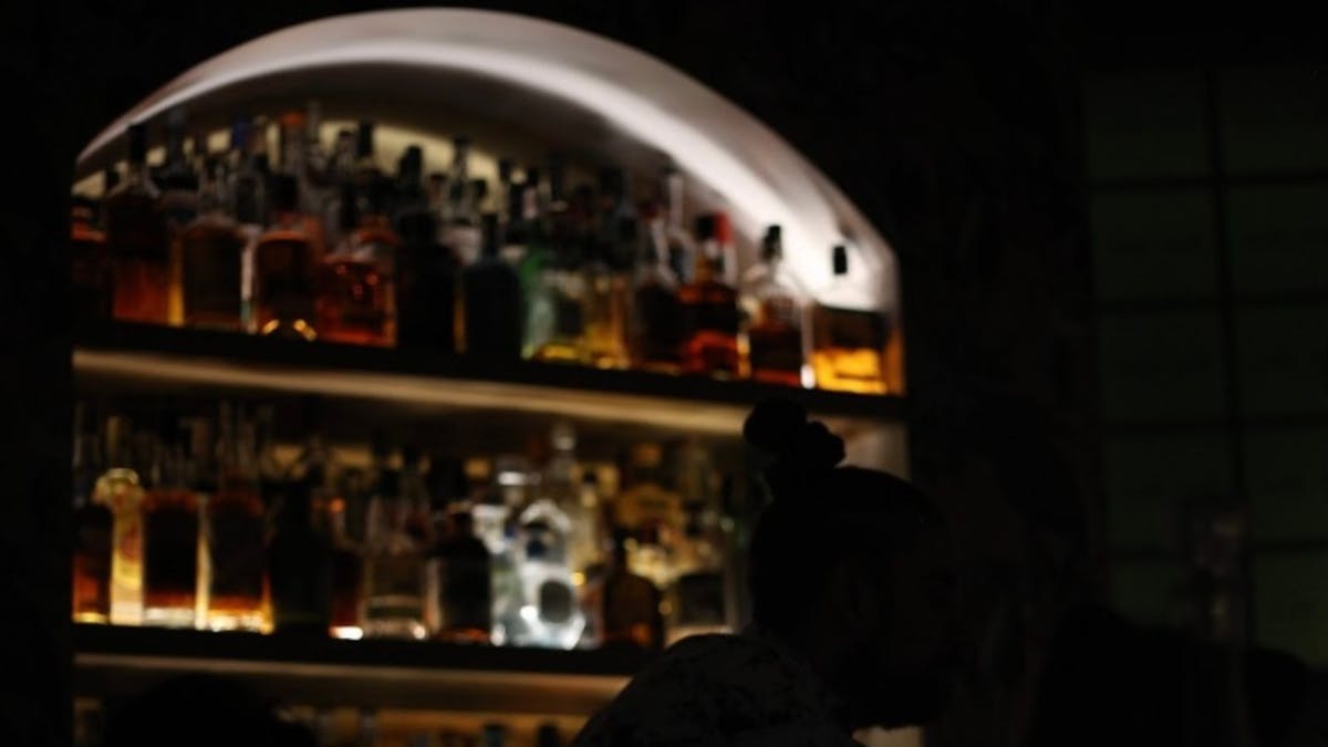 Silhouetted person standing in front of a lit backbar adorned with 100s of bottles
