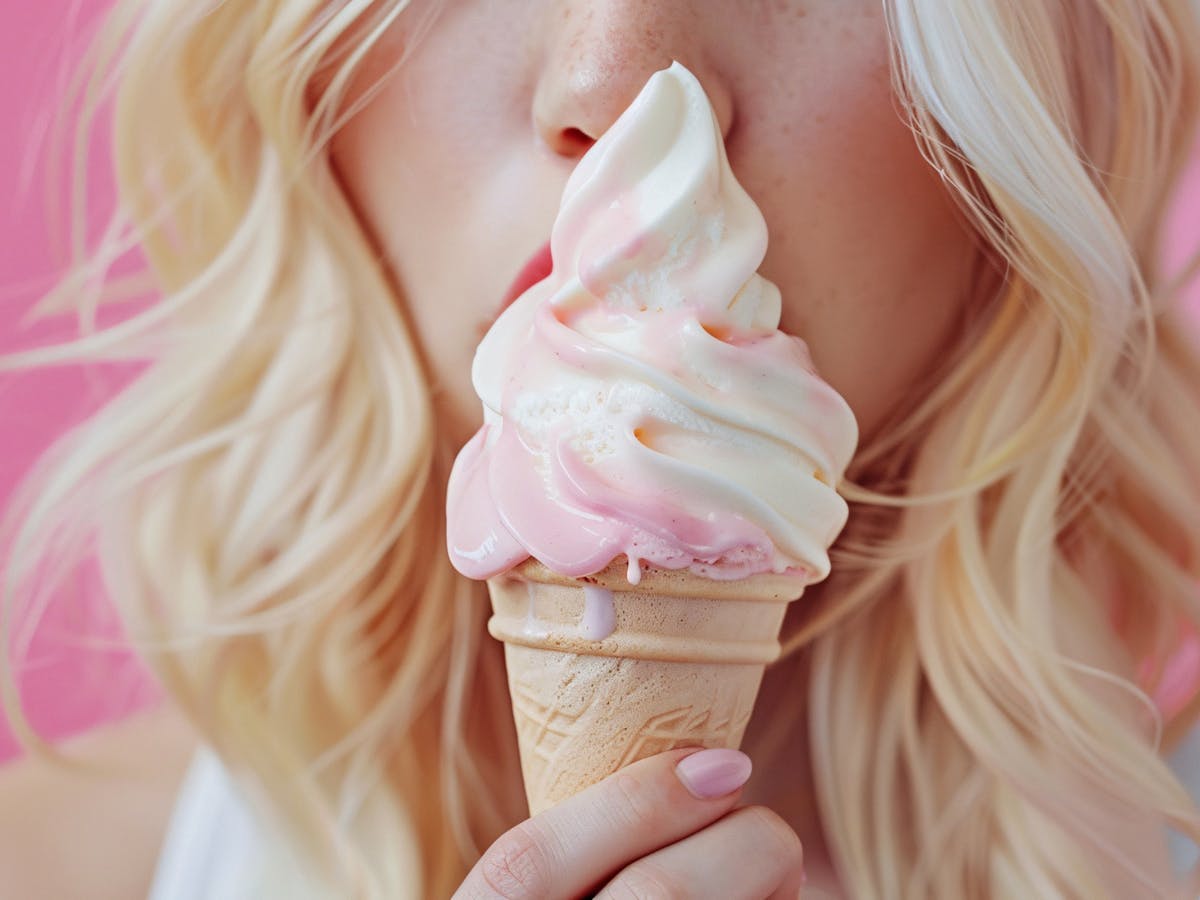 Close-up of a hand holding a pink and white swirled soft-serve ice cream cone