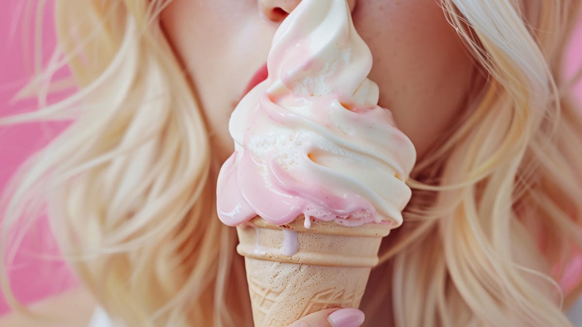 Close-up of a hand holding a pink and white swirled soft-serve ice cream cone Close-up of a hand holding a pink and white swirled soft-serve ice cream cone