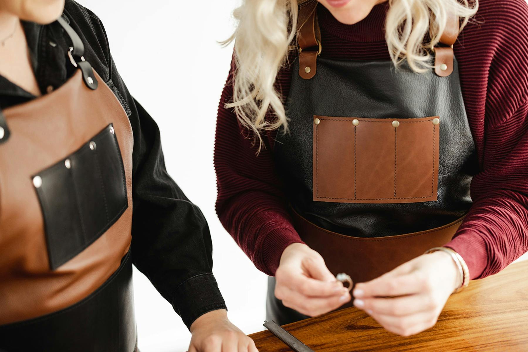 Two jewellers wearing leather aprons working together, focusing on a ring held in their hands