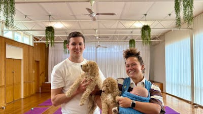Two smiling participants hold puppies in a Canberra studio with purple yoga mats.