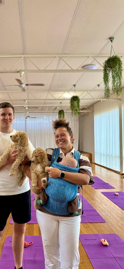 Two smiling participants hold puppies in a Canberra studio with purple yoga mats.