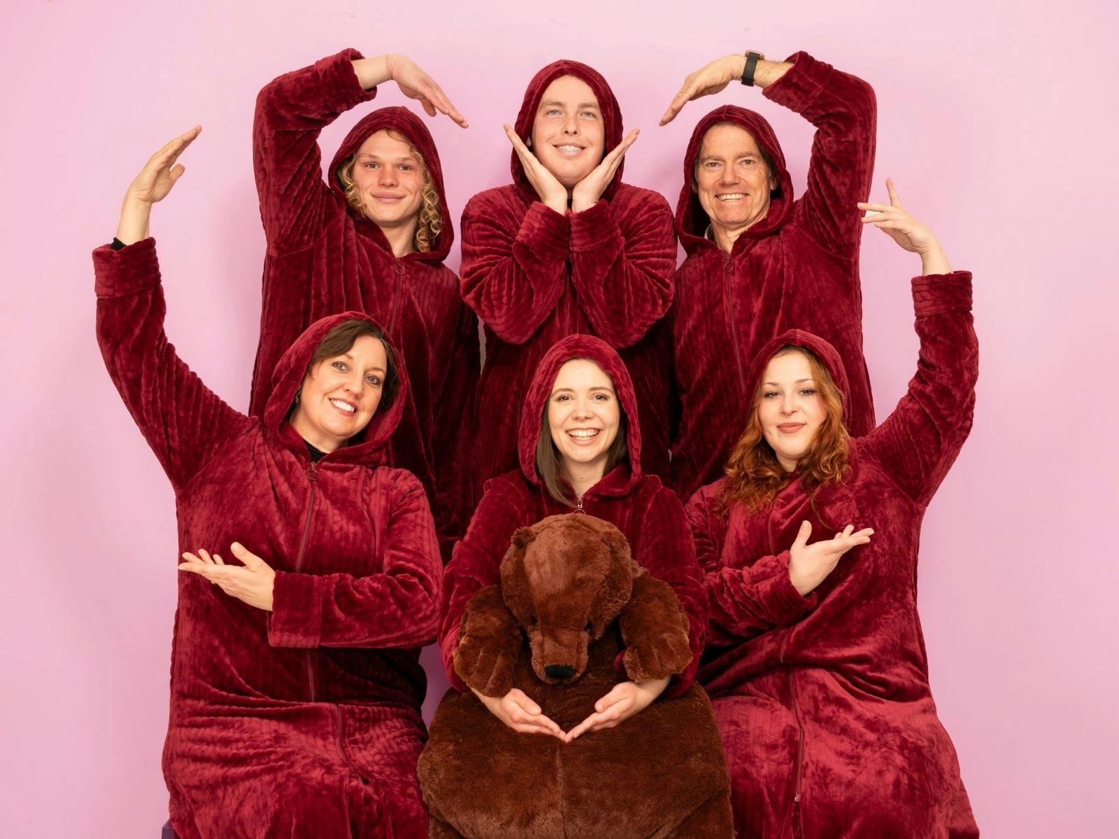 six people in plush red oodies smiling at the camera and making a heart shape by joining their hands