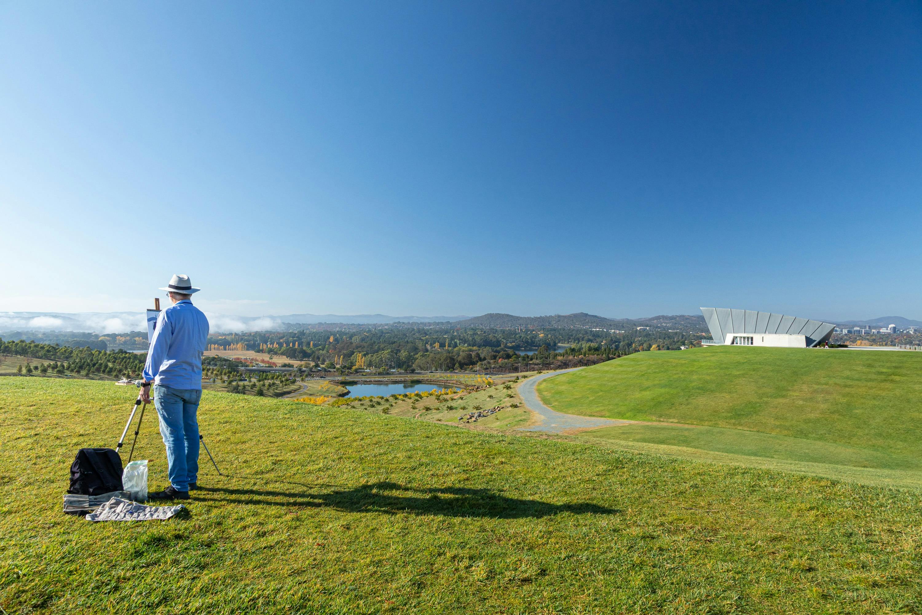 an artists easel with an artwork in front of a view of canberra and lake burley griffin