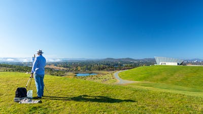 an artists easel with an artwork in front of a view of canberra and lake burley griffin