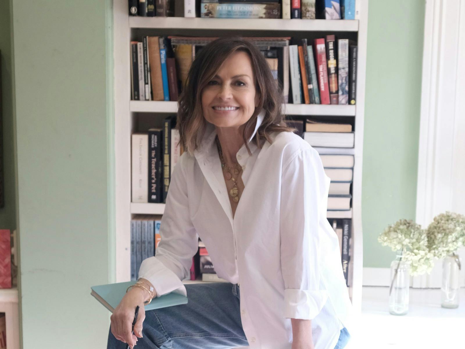 A woman sitting on a stool with a bookcase behind her