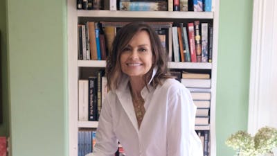 A woman sitting on a stool with a bookcase behind her