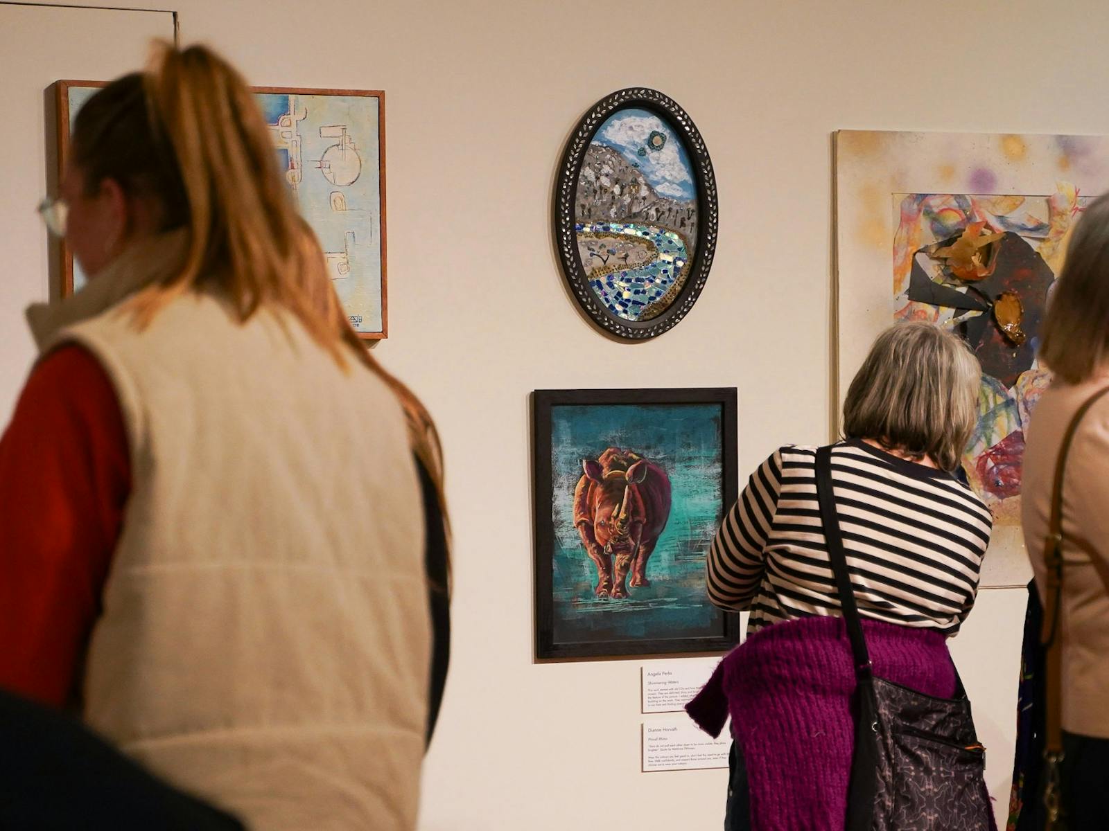 A visitor looks at two paintings on a wall, a rhino and a glass/mirror mosaic of a river