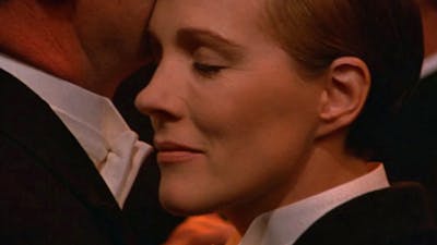 Close up of woman dressed in tuxedo with eyes closed pressed against chin of another person