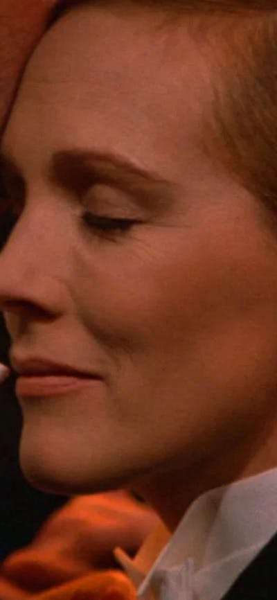Close up of woman dressed in tuxedo with eyes closed pressed against chin of another person