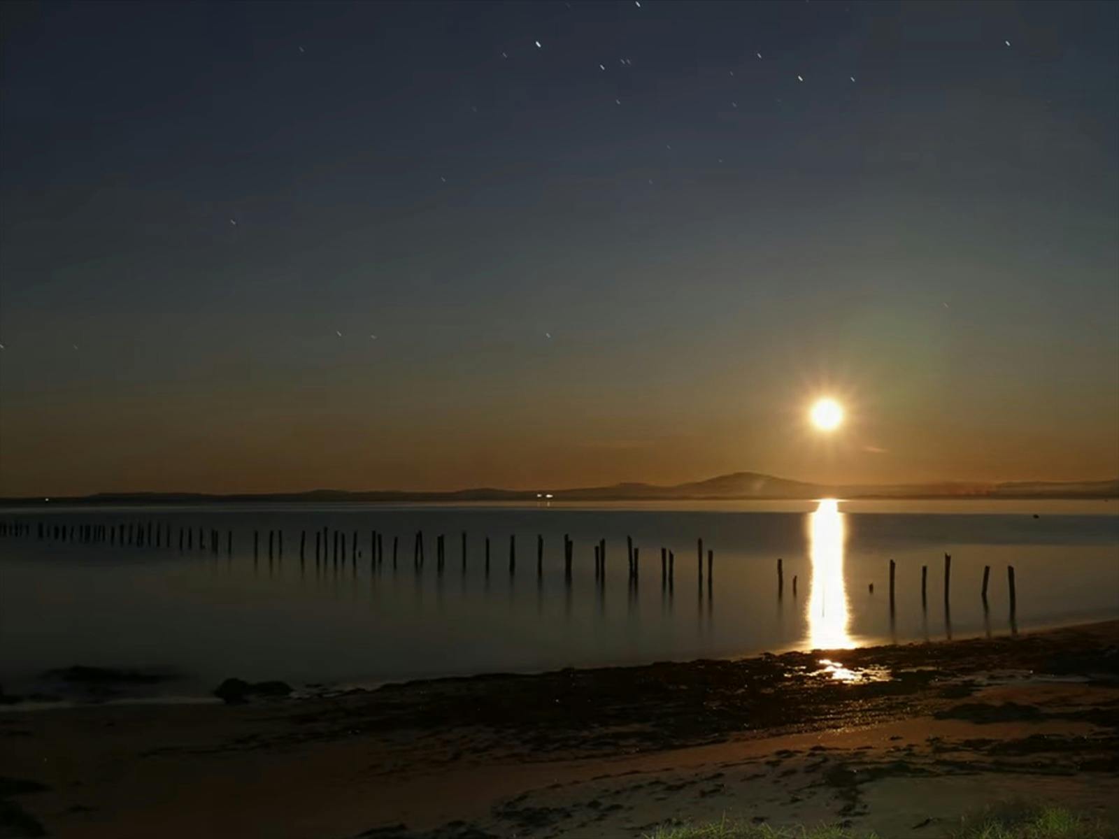 Sun setting low on the horizon, remnants of the old pier just visible in the low light
