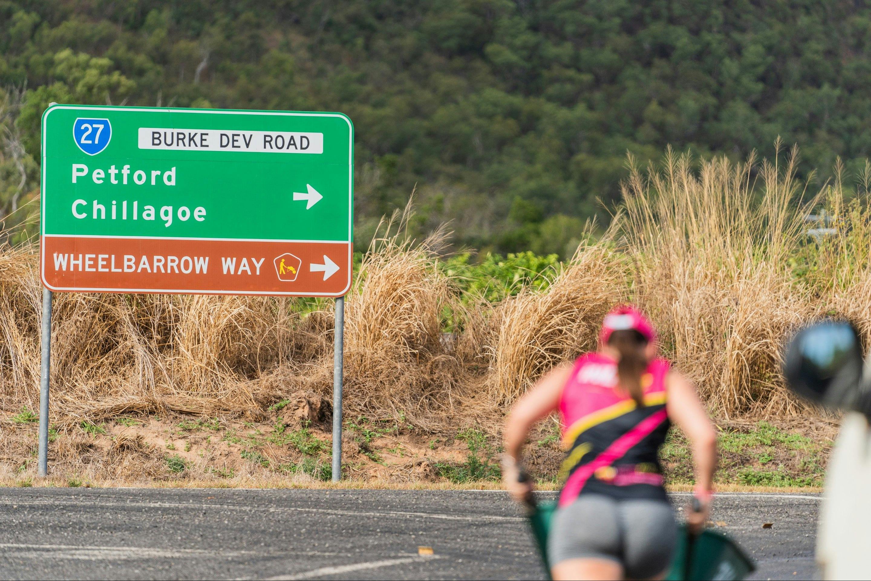 A woman in pink pushes a wheelbarrow along the great wheelbarrow way.