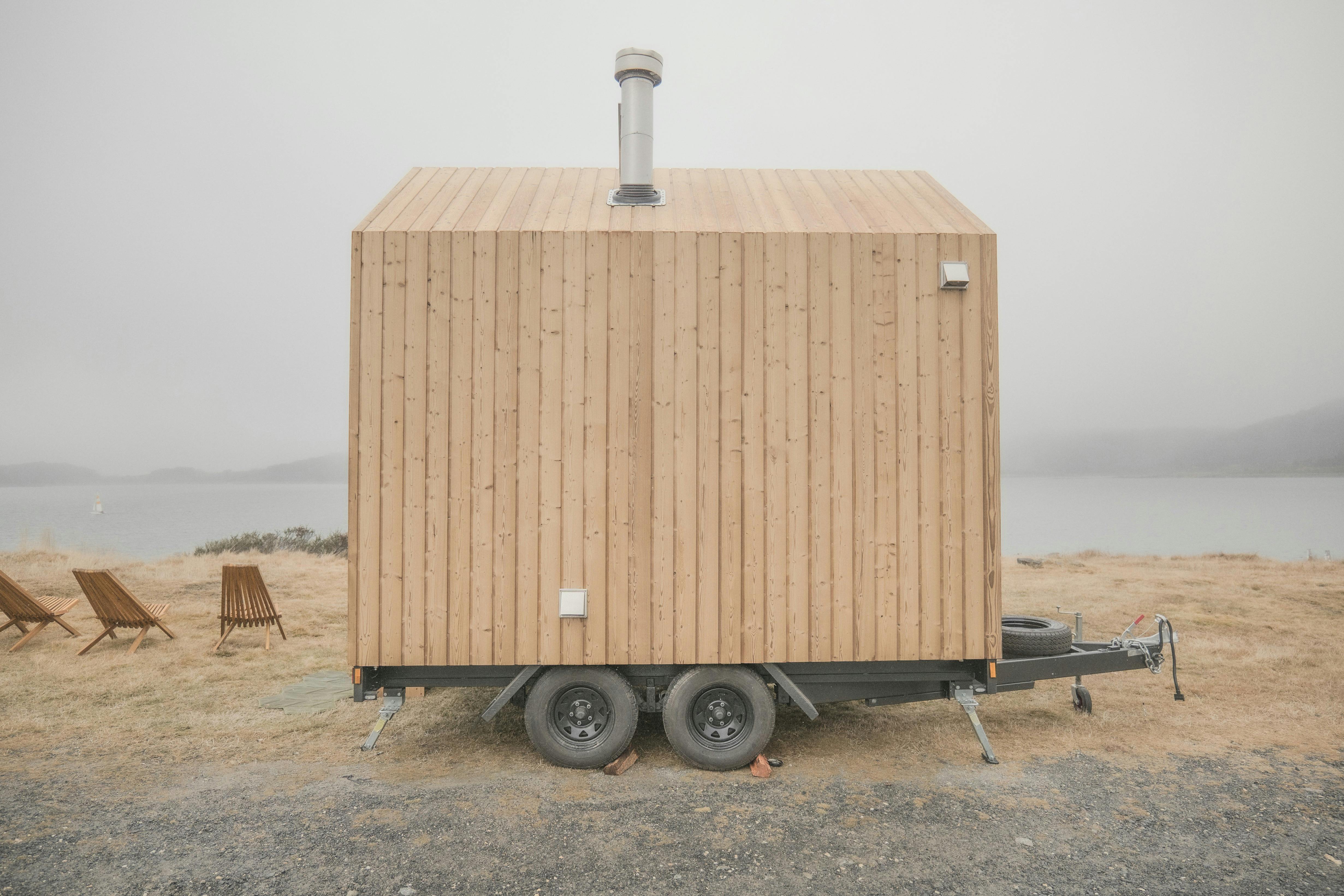Light wood coloured mobile nature sauna parked in front of  a lake view on a foggy day
