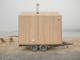 Light wood coloured mobile nature sauna parked in front of  a lake view on a foggy day