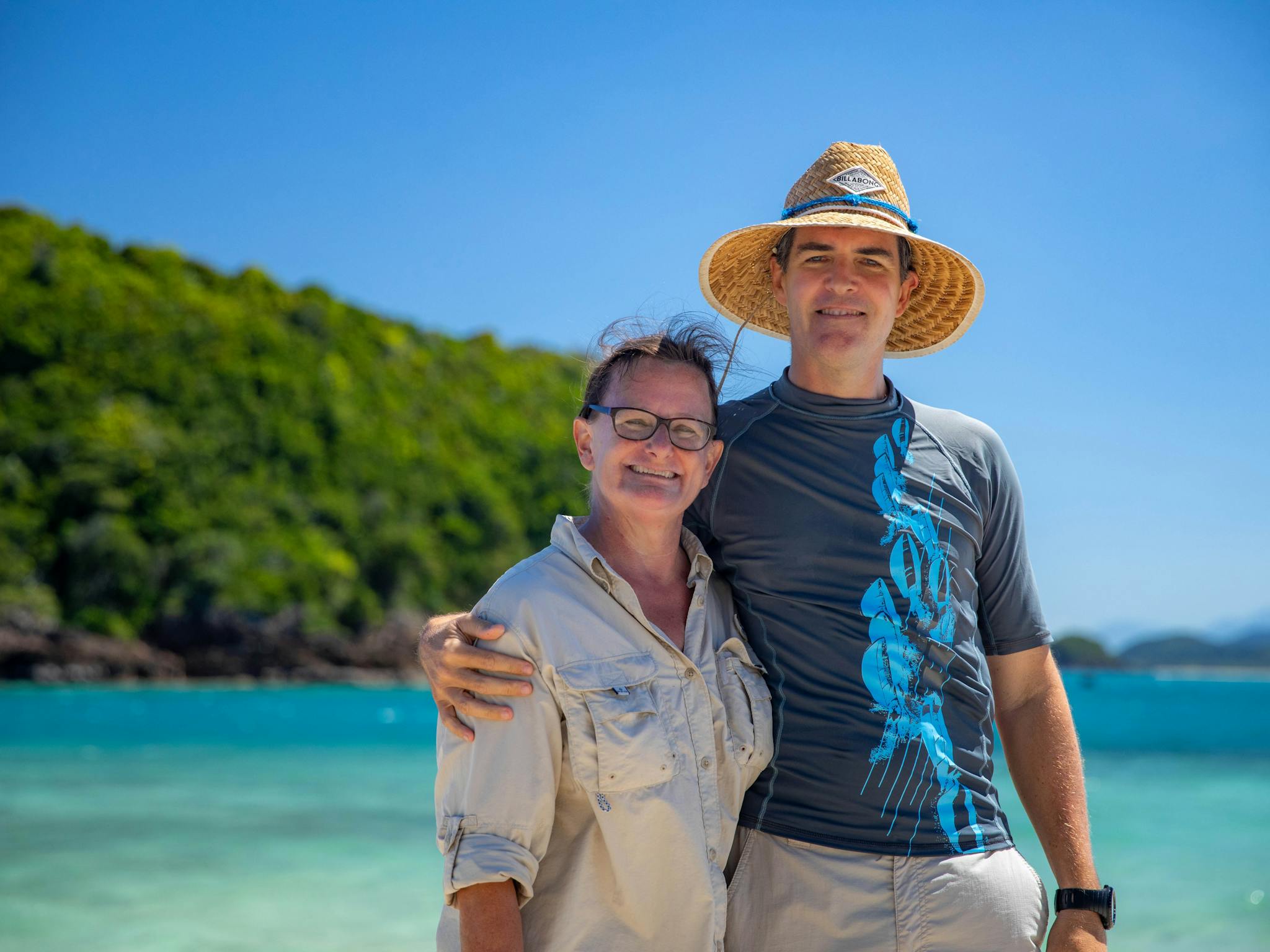A caucasian  womand and man are standing in front of a tropical island