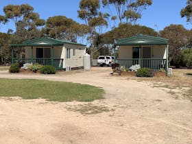 Two small, cream-coloured cabins with green trim sit side by side at Cummins Park and Cabin Park, ea