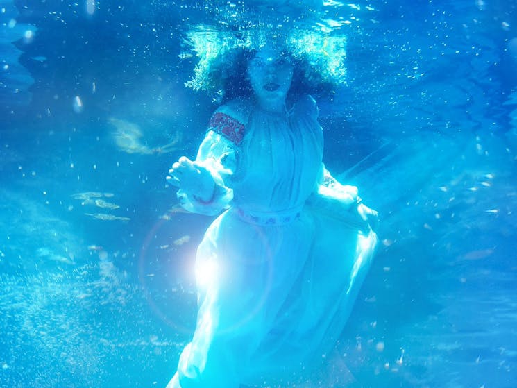 A girl in Ukrainian dress floats underwater, reaching forward
