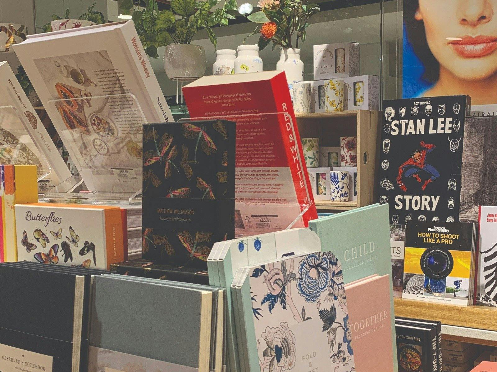 Boxed Stationary and books in foreground, ceramic tumblers and vases with botanical designs on raise