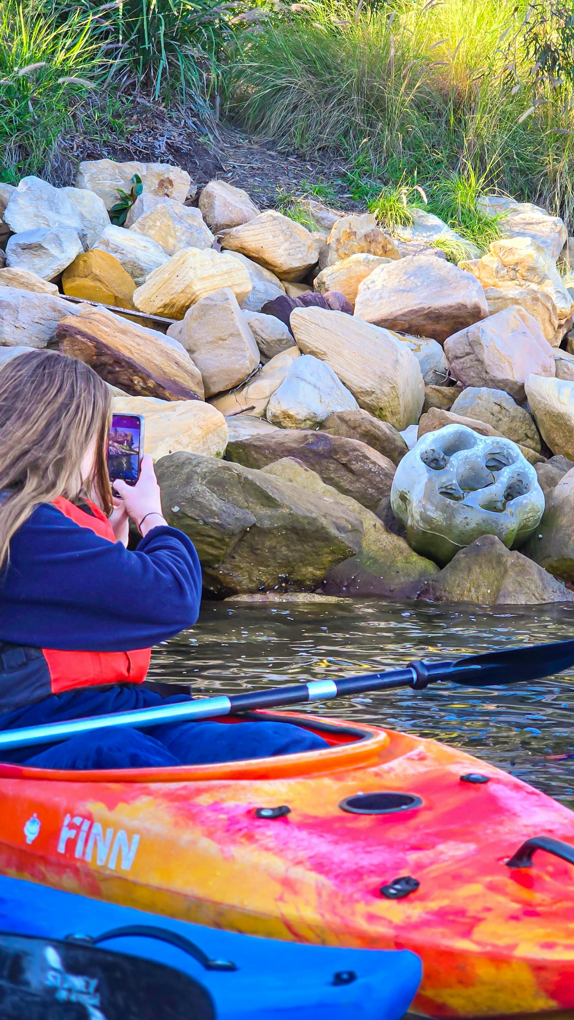 Dame mit roter Schwimmweste fotografiert mit ihrem Kamerahandy die Felsbrocken der Ufermauer