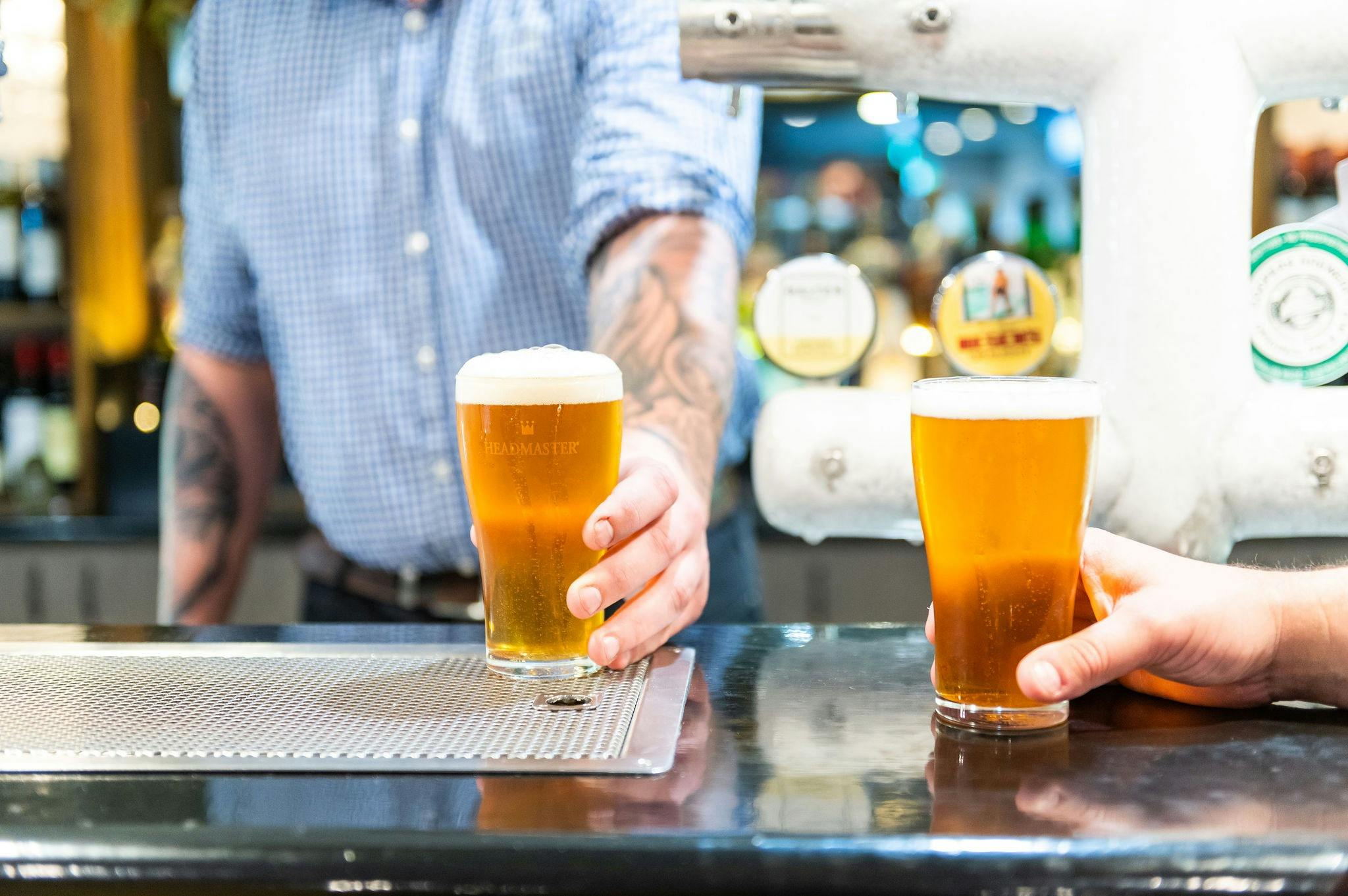 Man holding one beer as the bareman passes him a second schooner