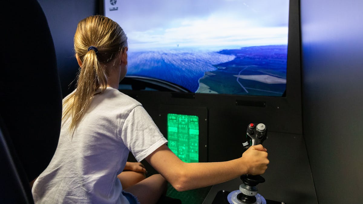 Child sitting in helicopter simulator chair holding a joystick and watching a TV screen