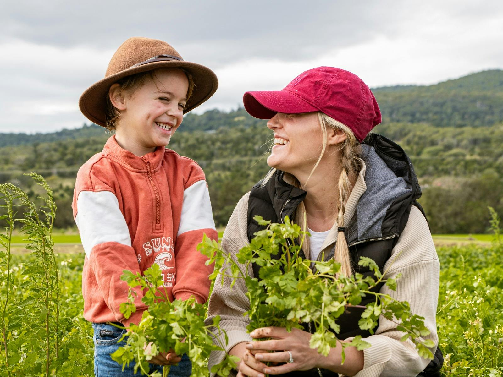 Mother and son standing in a field smiling at eachother holding a bunch of vegetables