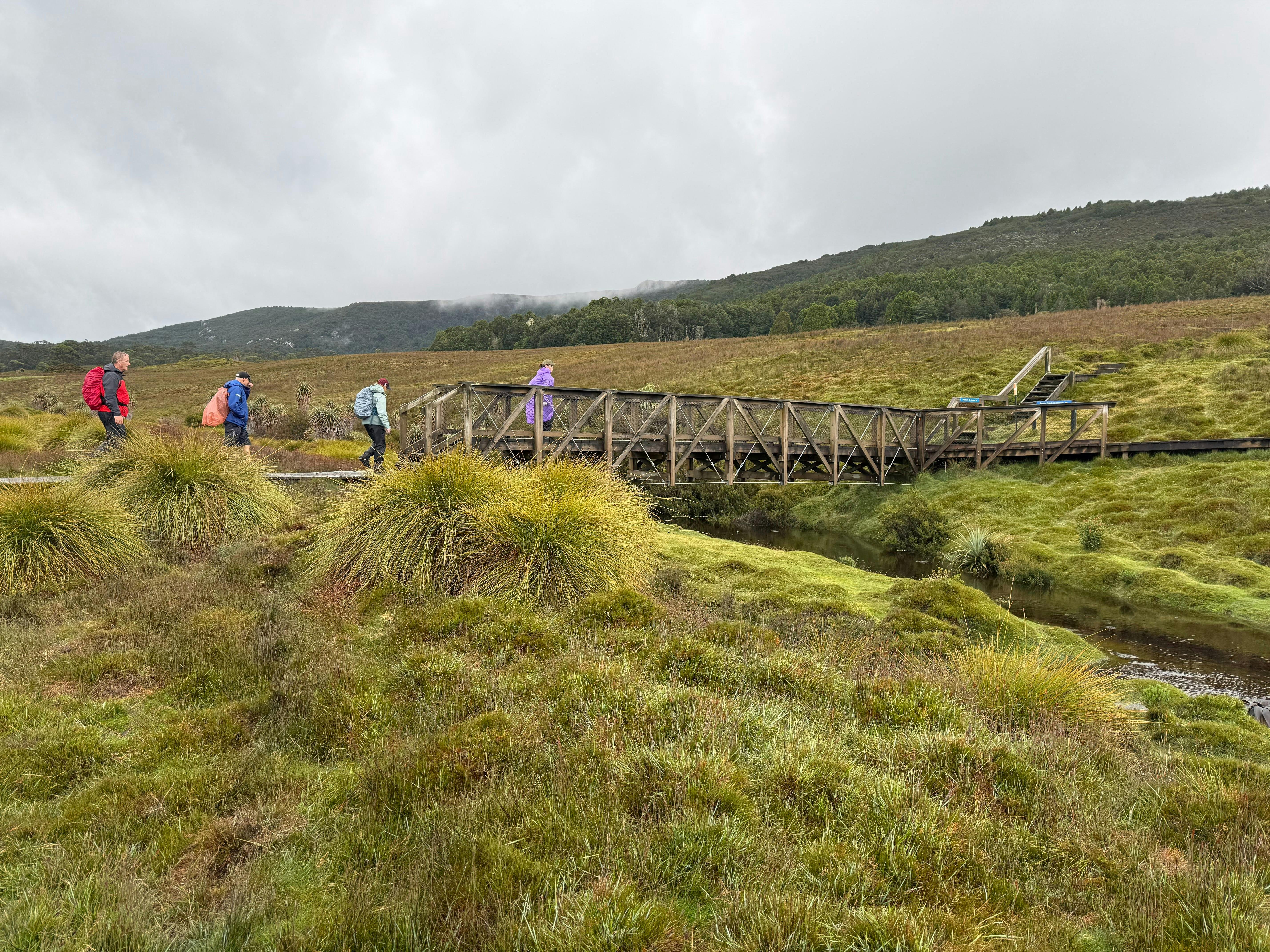 Walkers crossing a wooden bridge in alpine plains at Walls of Jerusalem National Park Tasmania.