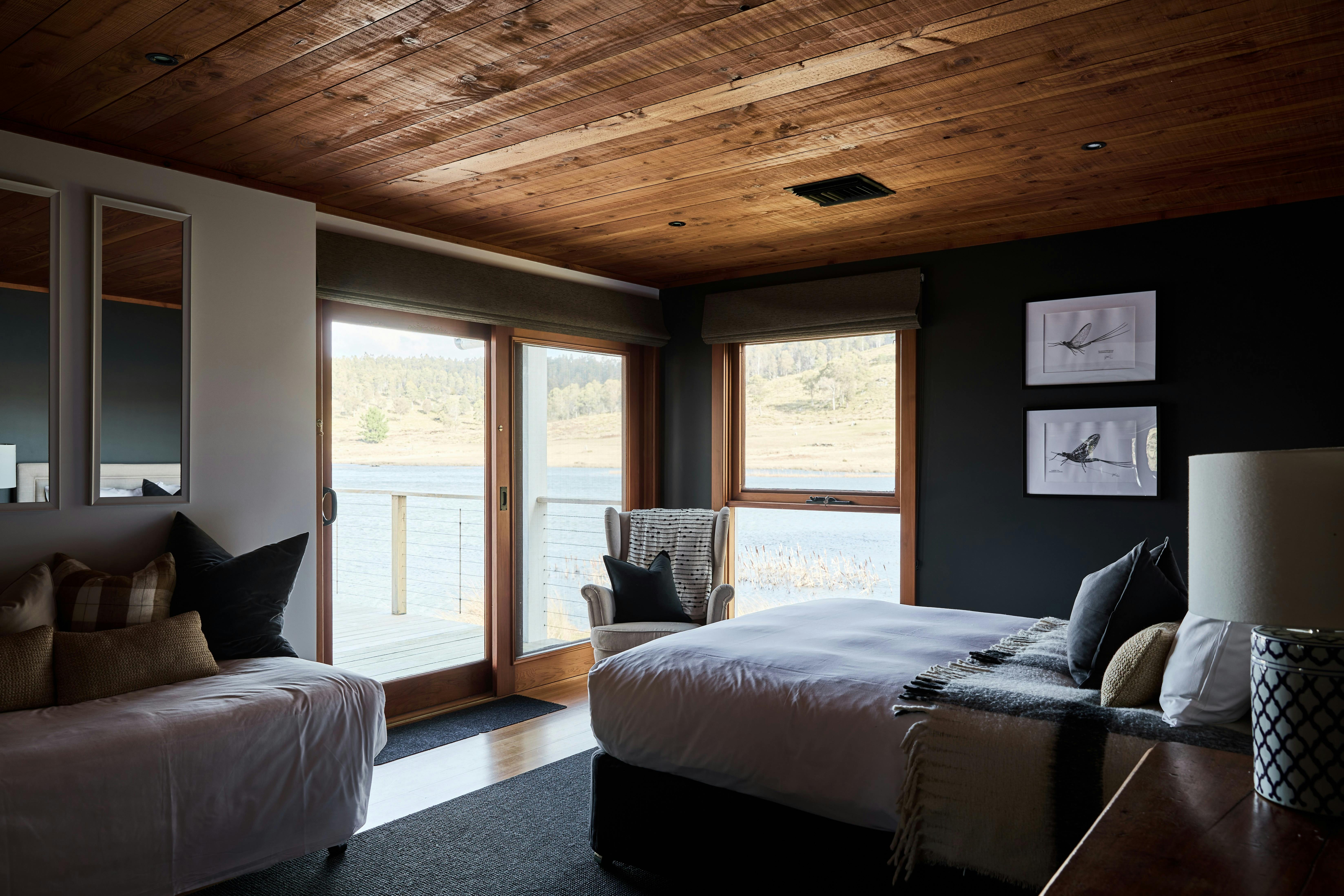 Queen and single bed in bedroom with glass door that accesses deck with lake views
