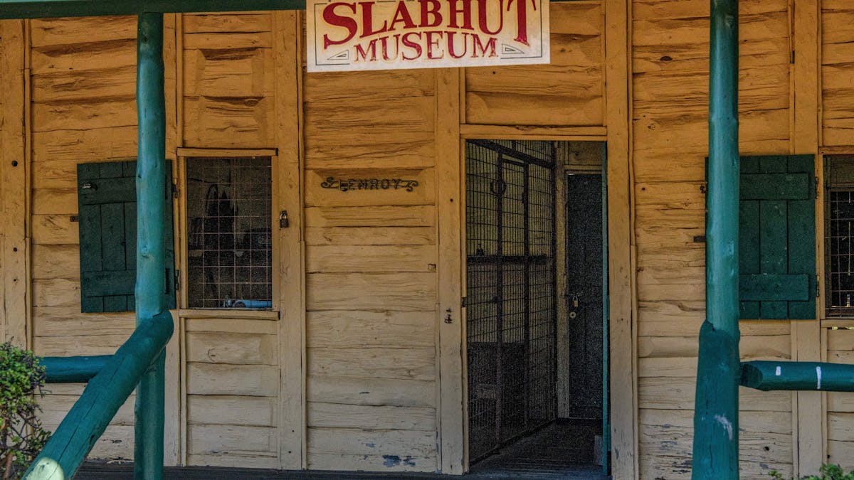 Entryway to a white wooden building. A sign reading 'Slabhut Museum'.